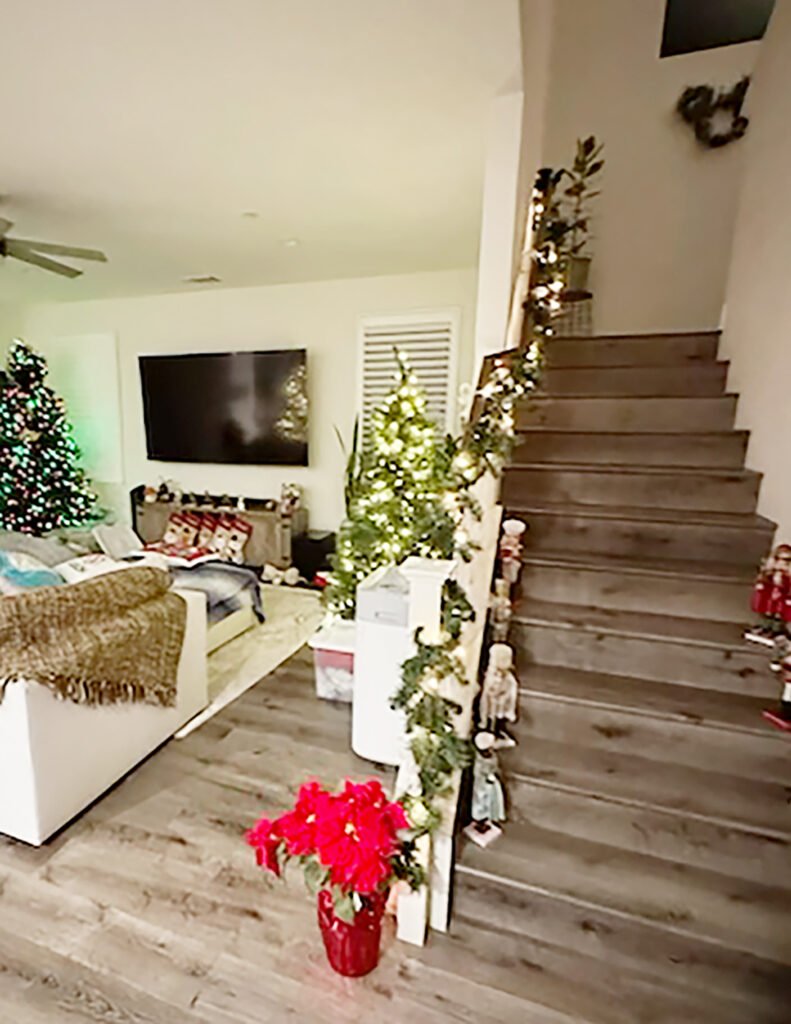 Home staircase decorated for Christmas with a lighted garland on the banister, nutcrackers on the steps, and a lit tree in the background.”